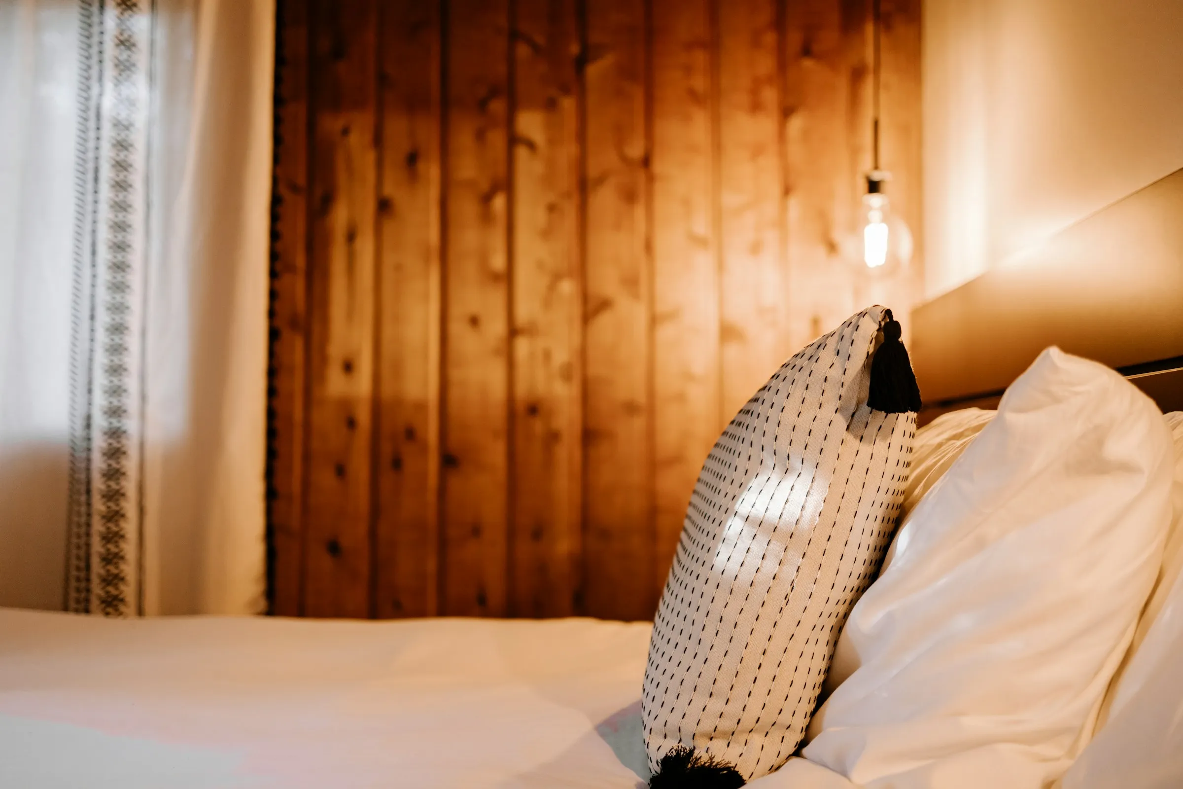 A made bed against a warm timber wall