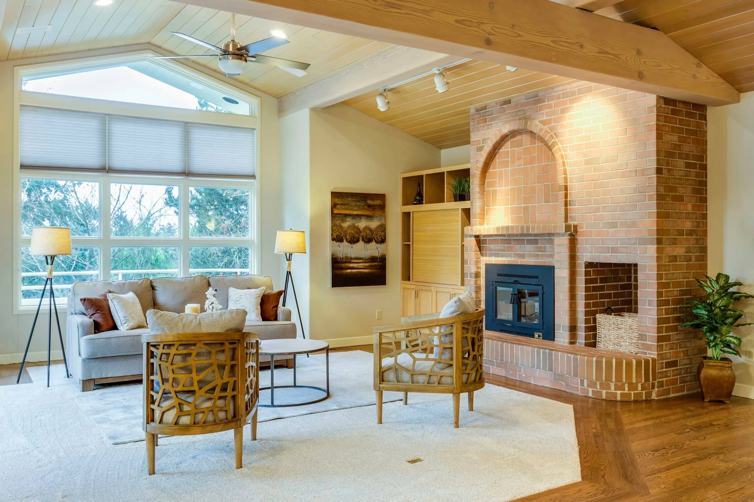 A bright great room with a timber ceiling and a brick fireplace