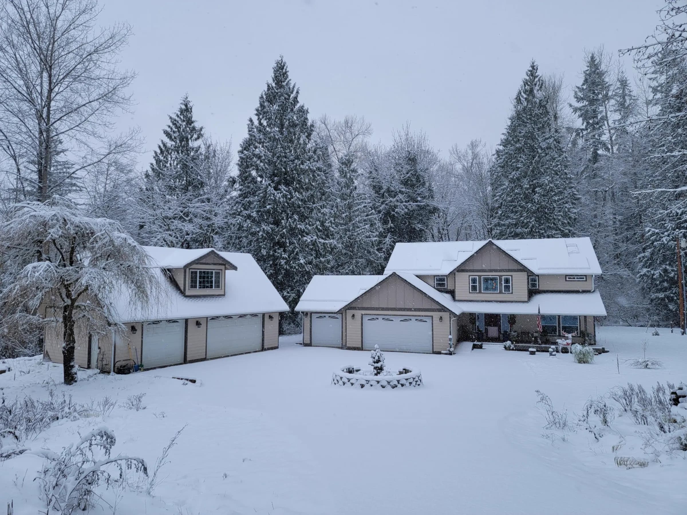 A lap-sided home and garage under fresh snow in the pines