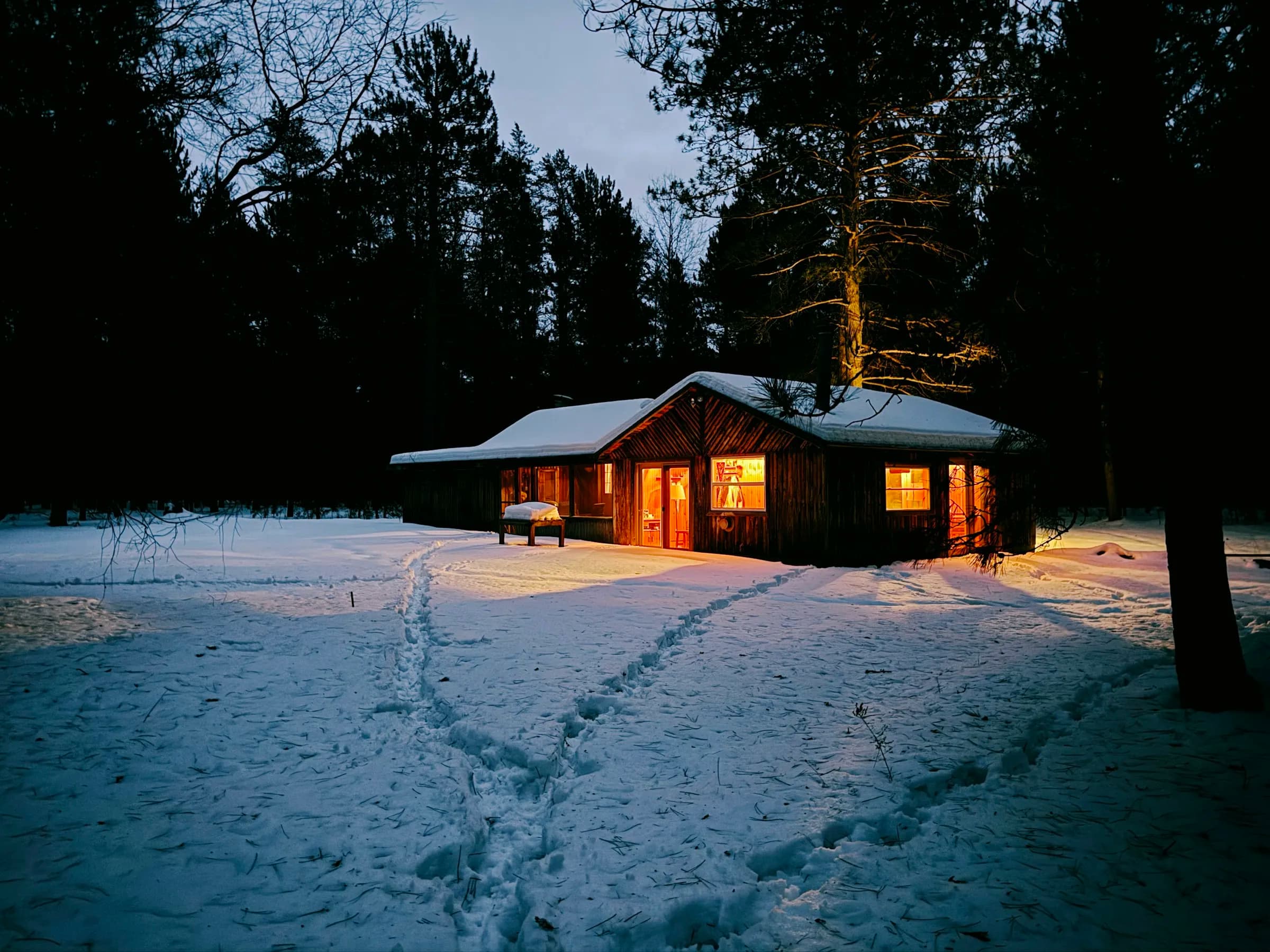 A cabin with lit windows in the snow at dusk